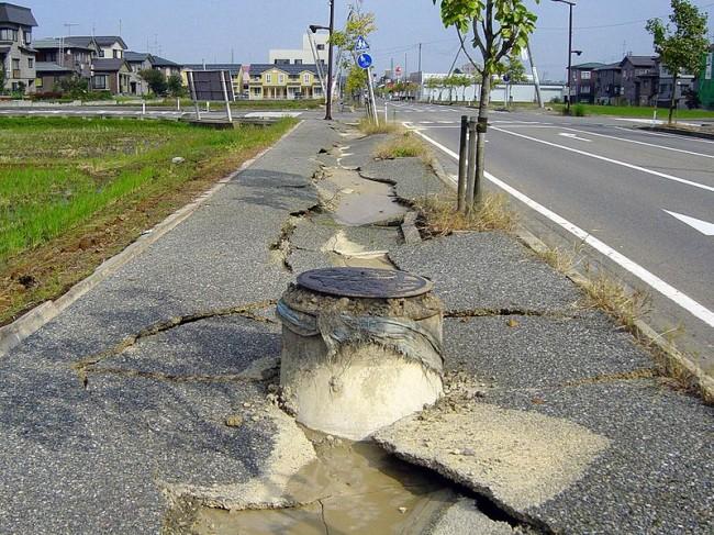 This photo shows just how much damage a strong earthquake can cause. The concrete pavement beside the street has been torn in two with a large crack down the middle.