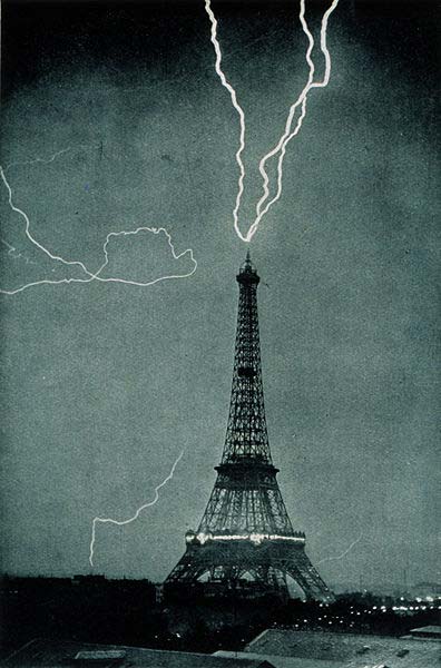 A black and white photo taken many years ago that shows a huge bolt of lightning hitting the top of the Eiffel Tower in Paris, France.