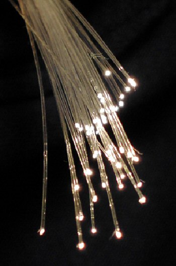 A number of strands of fiber optic cable emit a glowing light at the tips, the effect further enhanced by the black background.