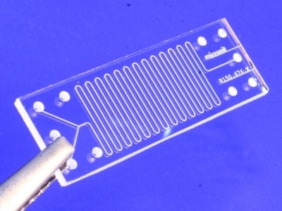 This photo shows a close up view of a glass microchip against a blue background.