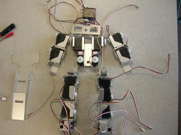 This photo shows a view looking down on a number of robot parts that combine to make a programmable robot that can perform complex movements. Some of the visible parts include wires, servo motors and metal brackets.