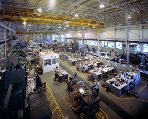 A large number of people can be seen hard at work in a large technology laboratory. The workers design and manufacture various technologically advanced products for use in various industries.