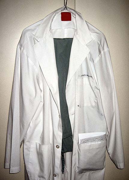 A new looking white lab coat hangs on the wall. Trousers hang on the inside and there are documents in the pocket.