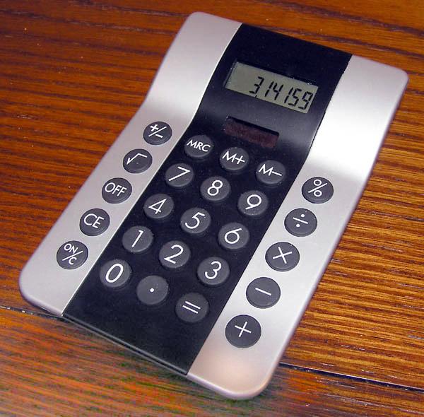 This photo shows a basic calculator sitting on a desk. The value of Pi is written to five decimal places on the screen.