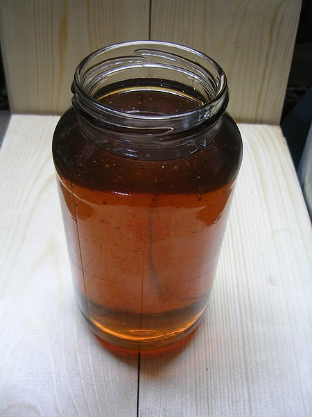 A glass jar is filled to near capacity with motor oil. The photo looks down from slightly above as the jar of motor oil sits on the table.